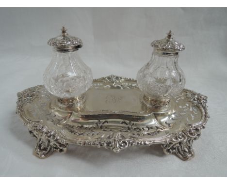 A Victorian silver ink stand having two cut glass ink wells of baluster form having hinged silver lids set on a pierced and m