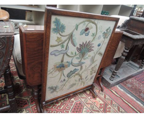 An early 20th century oak frame firescreen having crewelwork inset panel