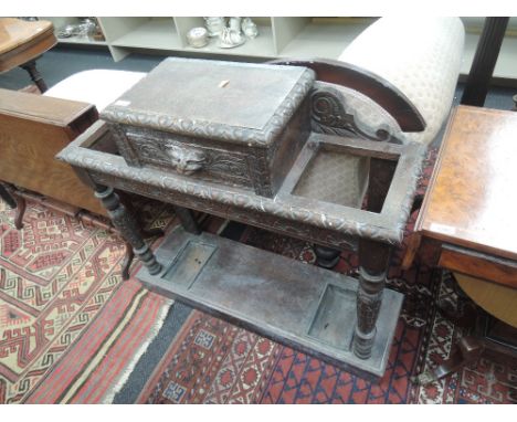 A late Victorian oak hall/stick stand having extensive carved decoration including mask head glove drawer, on foliate pillars