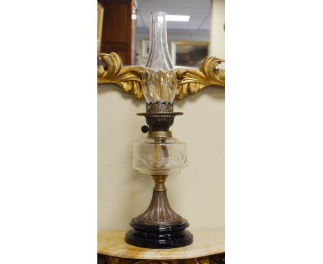 Victorian oil lamp having a clear cut glass reservoir and standing on a brass flared pillar with a black glazed ceramic base 