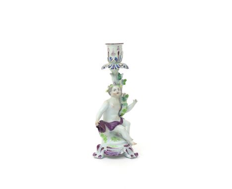 A Longton Hall candlestick figure of a putto  c.1755, seated and draped in a purple robe, leaning against a gnarled branch ap