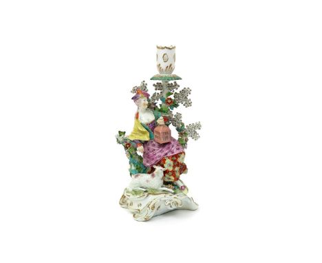 A Derby candlestick figure  c.1765, modelled as a lady leaning against flowering bocage, holding a birdcage in her left hand,