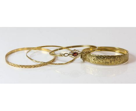 Four 9ct bangles, including two fixed carved bangles, one carved floral hinged bangles, and a bangle set with a garnet with a