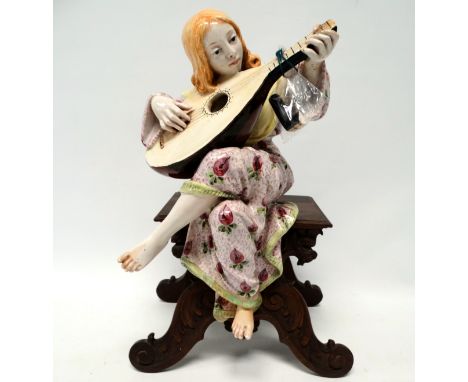 An early 20th century Arts &amp; Crafts style pottery figure - modelled as a woman playing a lute, mounted on a carved walnut