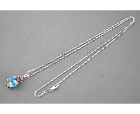 A white metal three stone pendant set with two garnets and a central blue topaz. Suspended from a rope link chain. Stamped 14