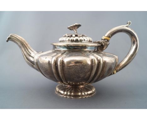 A silver squat form melon shaped teapot with fluted lid set with a cast floral and foliate handle over a lobed body with an i
