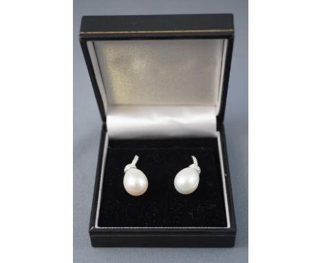 A white metal pair of drop earrings, each grain set with round cut diamonds and finished with a pear shape cultured freshwate