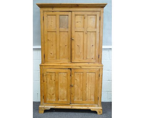 A pine two tier cupboard of plain rectangular form, the top with a shaped cornice with two x four panelled doors, the base wi
