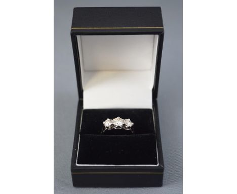 A white metal three stone ring, set with a central round brilliant cut diamond measuring approximately 5.50mm and further set