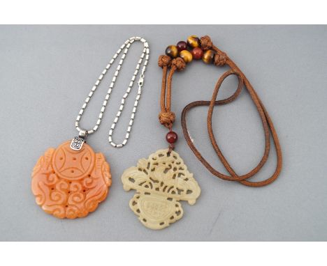A collection of two large carved pendants . One suspended from a brown beaded cord and one suspended from a silver chain. Tes