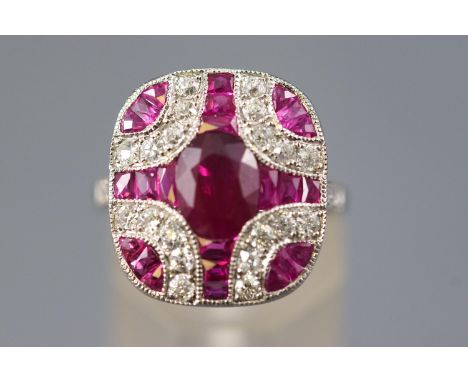 A white metal dress ring, set with an oval faceted cut ruby of approximately 1.30cts. Further set with calibre cut rubies and