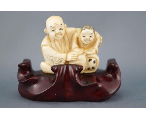 A late 19th century ivory netsuke of an old couple, seen seated and embracing, signed to the under-side, 4cm high