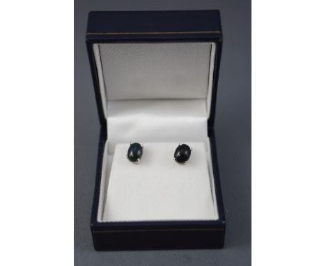 A white metal pair of single stone stud earrings, each set with an oval cabochon black Ethiopian opal. Post and scroll fittin