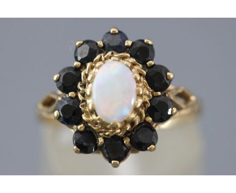 A yellow metal cluster ring set with an oval cabochon opal and surrounded by sapphires. Hallmarked 9ct gold, London. Size: N 