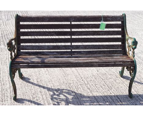 A cast metal and teak slat garden bench with arm supports finishing in a lion's mask, 78cm high x 127cm wide