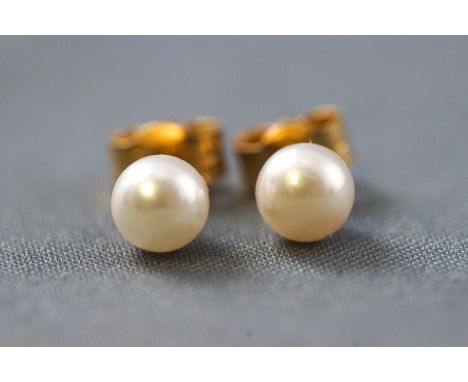 A yellow metal pair of single stone stud earrings each set with a 4.8mm cultured akoya pearl (untested). Post and scroll fitt