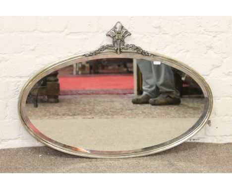 An oval metal framed bevel edged mirror with decorative pediment.