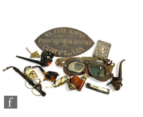 A collection of pipes to include ceramic examples, a pair of goggles, an oval dairy sign and assorted other items. (qty) 