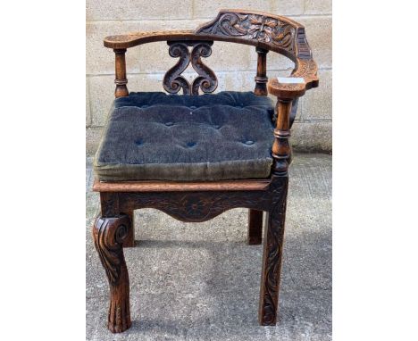 A 20th century oak corner chair, the back and arms profusely decorated with carvings of flora and fauna and a Green Man mask,