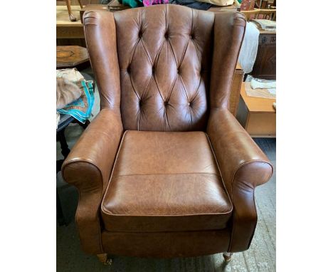 A modern mid brown leather wingback armchair, with button back, on four legs, the front two with casters, floor to seat heigh