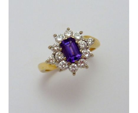 AN 18CT GOLD AMETHYST AND DIAMOND RING, with emerald cut amethyst within a surround of brilliant cut diamonds to the tapered 