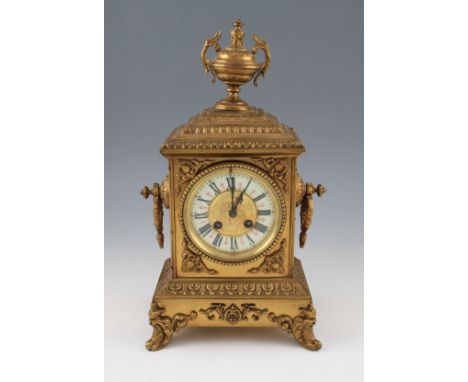 An early 20th Century brass mantel clock with ornate scroll decoration to body on four scroll feet with twin handled pedestal