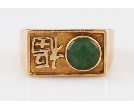 A yellow metal signet ring, rub over set with oriental circular green hard stone cabochon alongside an oriental character in 