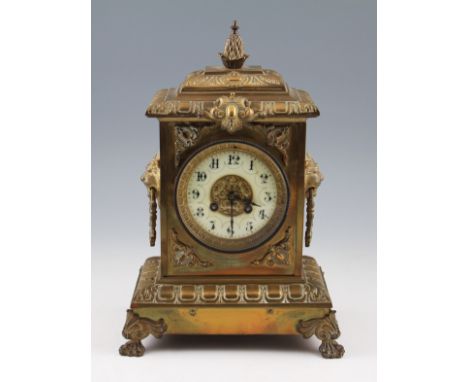 An early 20th Century brass mantel clock with lion head bust handles to sides with scroll design front, all on four raised fe