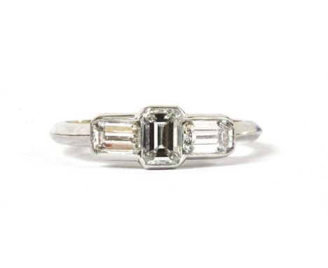 A platinum three stone emerald cut diamond ring, an emerald cut diamond in portrait orientation, flanked either side by an em