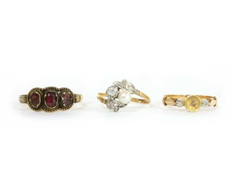 A gold three stone garnet ring, a row of oval mixed cut garnets, chipped, claw set to twisted wire frames and 'D' section sha