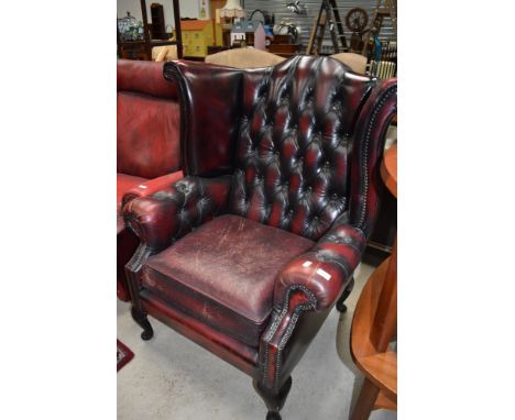 A 20th century wing back arm chair having button back ox blood leather