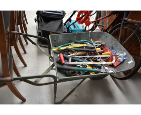 A wheel barrow containing a mixed lot of hand tools.