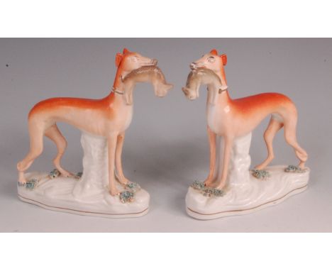 A pair of mid-Victorian Staffordshire hunting hounds, each modelled with a hare in its muzzle, decorated in naturalistic colo