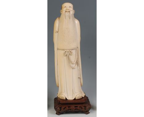 An early 20th century Chinese carved ivory figure of a robed scholar, holding beads behind his back, with penwork decoration,