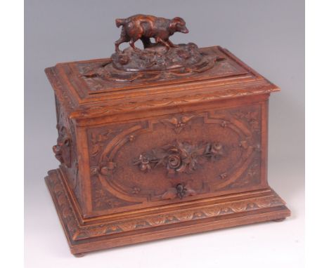 A late 19th century Black Forest carved walnut tantalus box, the cover surmounted with a hound amidst foliage, opening to rev