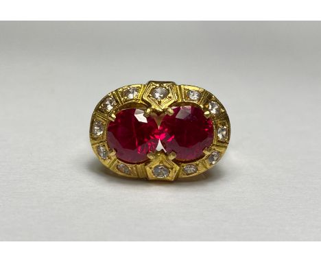 A striking synthetic ruby dress ring, the two round-cut rubies claw-set within a band of round brilliant-cut colourless stone