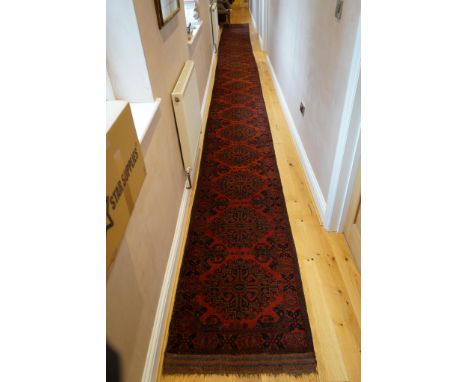 A large Pakistani Bokhara motif hand-knotted wool red ground runner, approx. 950 x 72cm. Condition - fair to good