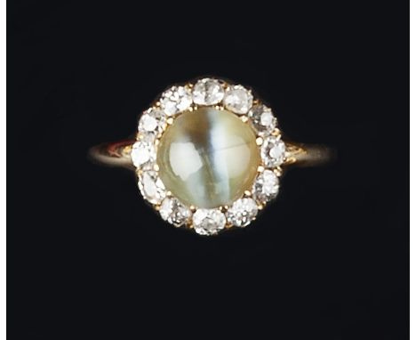 A CHRYSOBERYL CAT'S EYE AND DIAMOND CLUSTER RING, the circular cabochon chrysoberyl cat's eye in claw setting, within a borde