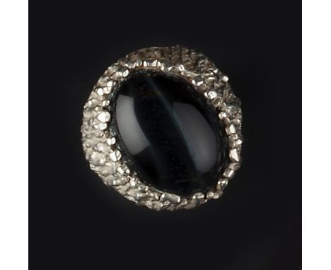 A SILVER AND GEM SET MODERNIST RING BY PETER GUY WATSON, of textured abstract design, centred with an oval cabochon treated b