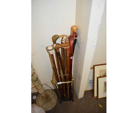 Brass stick stand containing an assortment of various walking sticks to include examples with carved heads