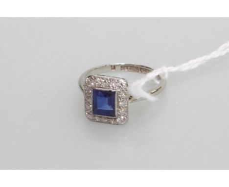 A sapphire and diamond cluster ring in the Art Deco taste, the collet-set sapphire within a band of round brilliant-cut diamo