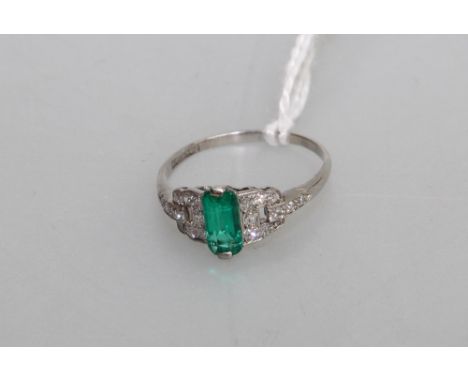 An emerald and diamond ring in the belle epoch taste, the central emerald cut emerald 0.63cts, on a platinum band, ring size 