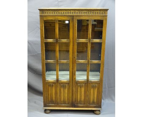 A VINTAGE OAK DISPLAY CABINET with twin glazed panel and linenfold carved doors, on bun feet, 135cms high, 79cms wide, 35cms 