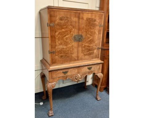A 20th century burr walnut cocktail cabinet with two doors enclosing glass and mirror interior and pull out shelf above two d