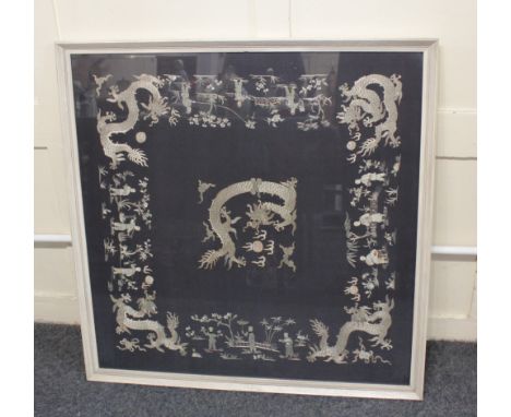 A framed Chinese embroidered black silk panel, possibly a shawl, decorated with a dragons and flaming pearls amongst figures 