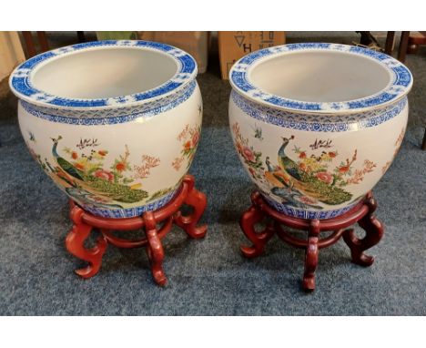 A pair of modern Oriental ceramic jardineres on wooden stands, each decorated with peacocks and other birds amongst flowering