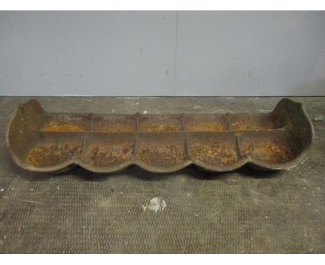 A vintage cast iron pig trough divided into ten feeders.