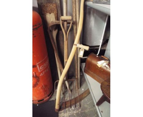 A selection of vintage farm tools including a scythe, pitchforks, drainage scoops, potato forks etc