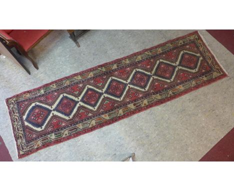 Ab Afghan runner with seven diamond pole medallions on a red ground, within border of geometric motifs on a cream ground, 288
