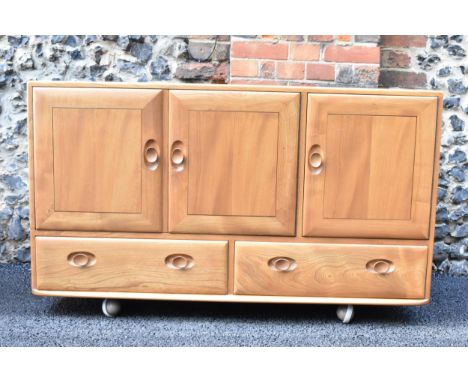 A mid 20th century Ercol Windsor range light elm sideboard, mode 468, having three cupboard doors above two short drawers, ra